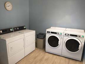 A laundry room with a clock on the wall and two washing machines.
