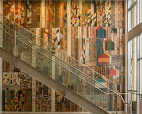 A staircase with a glass railing and a mosaic wall on the side.
