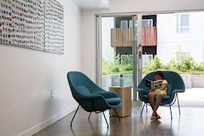 A woman is sitting on a blue chair reading a book.