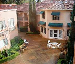 A patio with a table and chairs is surrounded by bushes and trees.