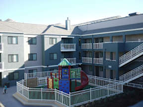 A playground with a slide and a climbing frame in front of a building.