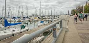 A marina with boats docked and people walking on the sidewalk.