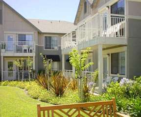 A wooden bench is in front of a building with a balcony.