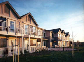 Apartment complex with balconies and a small garden in front.