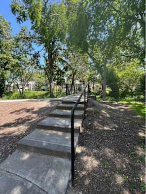 A set of stairs with a metal handrail lead up a tree-lined path.