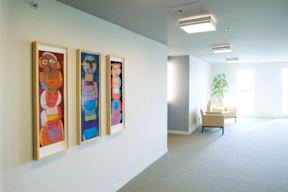 Three paintings hang on a wall in a white room.