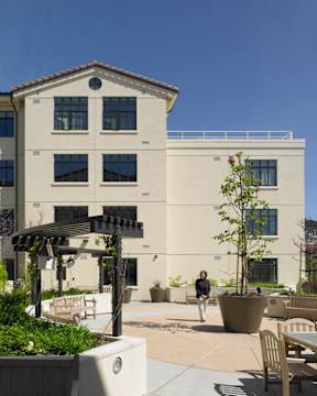 A woman walks past a tree in front of a building.