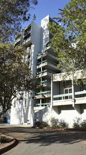 A white building with green balconies and trees in front.