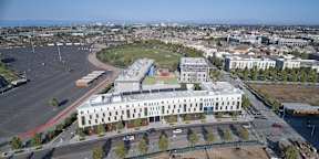 A large white building with a green roof is surrounded by a parking lot.