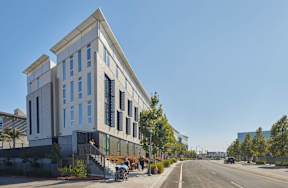 A modern building with a glass facade is situated on a street with a clear blue sky above.