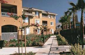 A row of apartment buildings with a sidewalk in front.