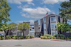The image shows a modern building with a flag on top, surrounded by greenery and trees.