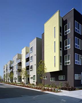 A row of modern apartment buildings with balconies and trees in front.