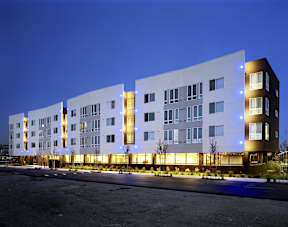 A modern building with white and brown exterior and lights on.