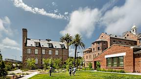 A large building with a clock tower is surrounded by a green lawn.