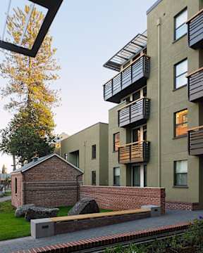 A modern apartment building with balconies and a small brick building in the foreground.