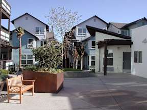 A wooden bench sits in front of a house with a planter in front of it.