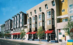 A row of modern apartment buildings with red awnings line a street.