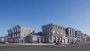 A street view of a row of buildings with cars parked in front.