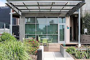 A modern building with a glass facade and a wooden deck with chairs and plants.
