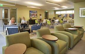 A group of people sitting in a room with green chairs and tables.
