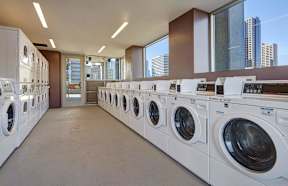 A laundromat with rows of washing machines and a view of the city outside the windows.