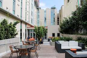 A patio with a table and chairs is surrounded by buildings and greenery.
