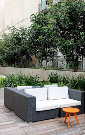 A black wicker sofa with white cushions and an orange stool on a wooden deck.