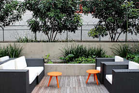 A patio with a black wicker sofa, a small orange table, and a white cushion.