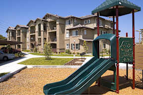 A playground with a green slide in front of apartment buildings.