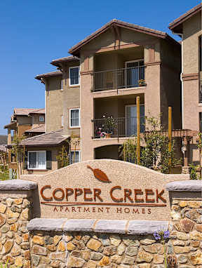 A stone wall with a sign that says Copper Creek Apartment Homes.