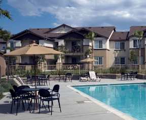 A pool area with chairs and umbrellas in front of apartment buildings.