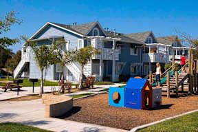 A playground with a slide and a playhouse in front of a row of houses.