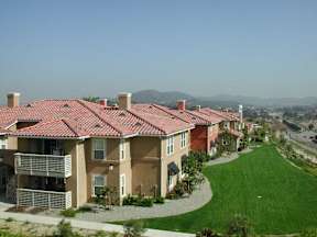 A row of houses with red roofs and green lawns.
