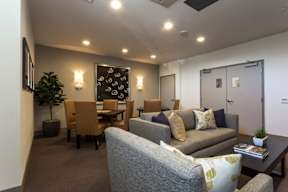 A living room with a grey couch, a wooden dining table, and a potted plant.