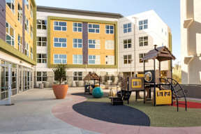 A playground area with a slide, ball pit, and climbing wall in front of a multi-story building.