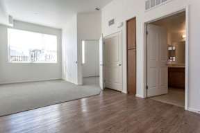 A room with white walls and wooden floors has a rug on the floor and a door on the right.