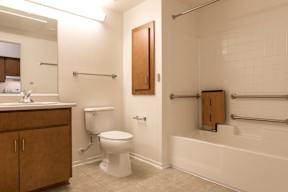 A white toilet is in a bathroom with a white tub.