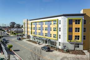 A modern building with yellow and grey exterior is surrounded by a parking lot.