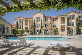 A pool surrounded by sun loungers and apartment buildings.