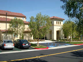 A building with a red tile roof and a white tower with a balcony is surrounded by trees and cars.