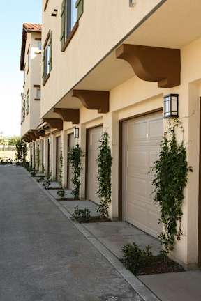 A row of houses with garages and plants on the side.