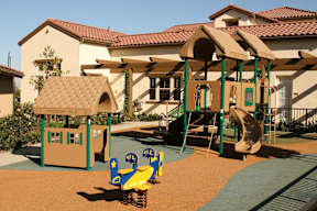 A playground with a yellow and blue slide and a green and yellow swing set.