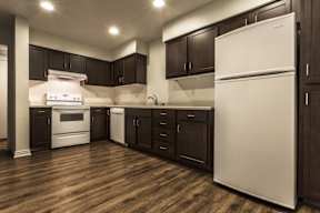 A white refrigerator stands in a kitchen with dark wood floors and cabinets.