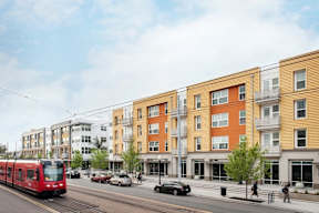 A red train is on the tracks in front of a row of buildings.