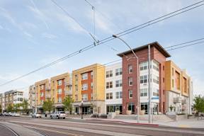 A street view of a multi-story building with a red brick facade and a yellow section on the ground floor.