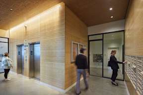 Two people are walking through a hallway with a wooden wall and glass doors.