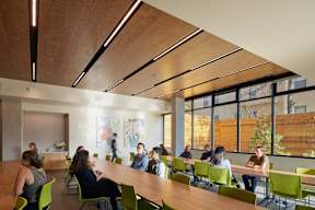 A group of people are sitting around a table in a room with a wooden ceiling.