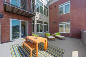 Apartments for Rent San Rafael - Second and B Street - Private Balcony with a Table and Two Benches Over a Large Rug, Two Chairs with Their Own Footrests, and a Sliding Glass Door Leading to the Bedroom