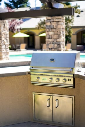 an outdoor kitchen with a grill and a pool in the background